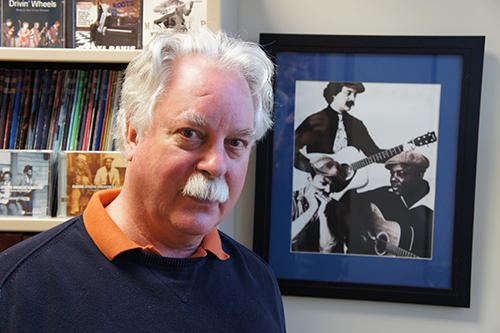 Dr. Barry Lee Pearson in his office at the University of Maryland. Behind him hangs a photo during the time when he played with John Cephas and Phil Wiggins.