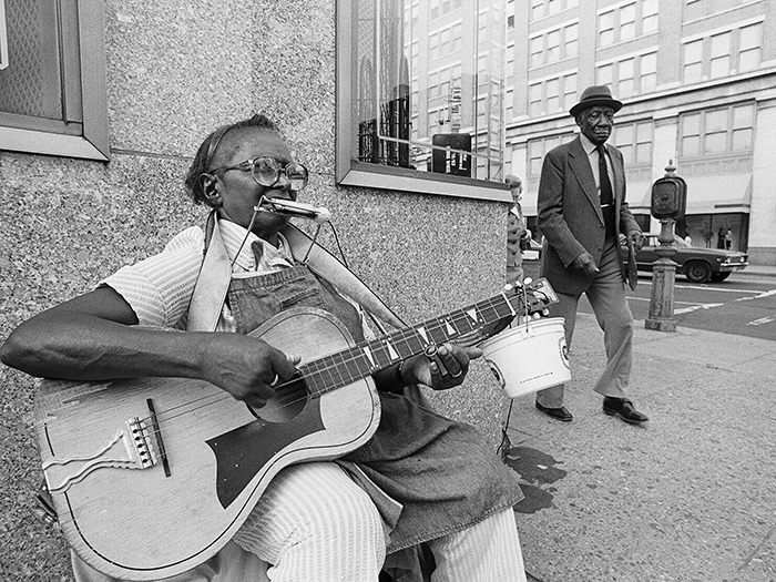 woman playing guitar and harmonica on street